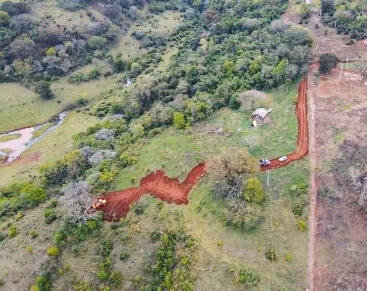 Fotografia aérea da chácara durante um período de terraplanagem, mostrando áreas de vegetação, declive e acesso interno